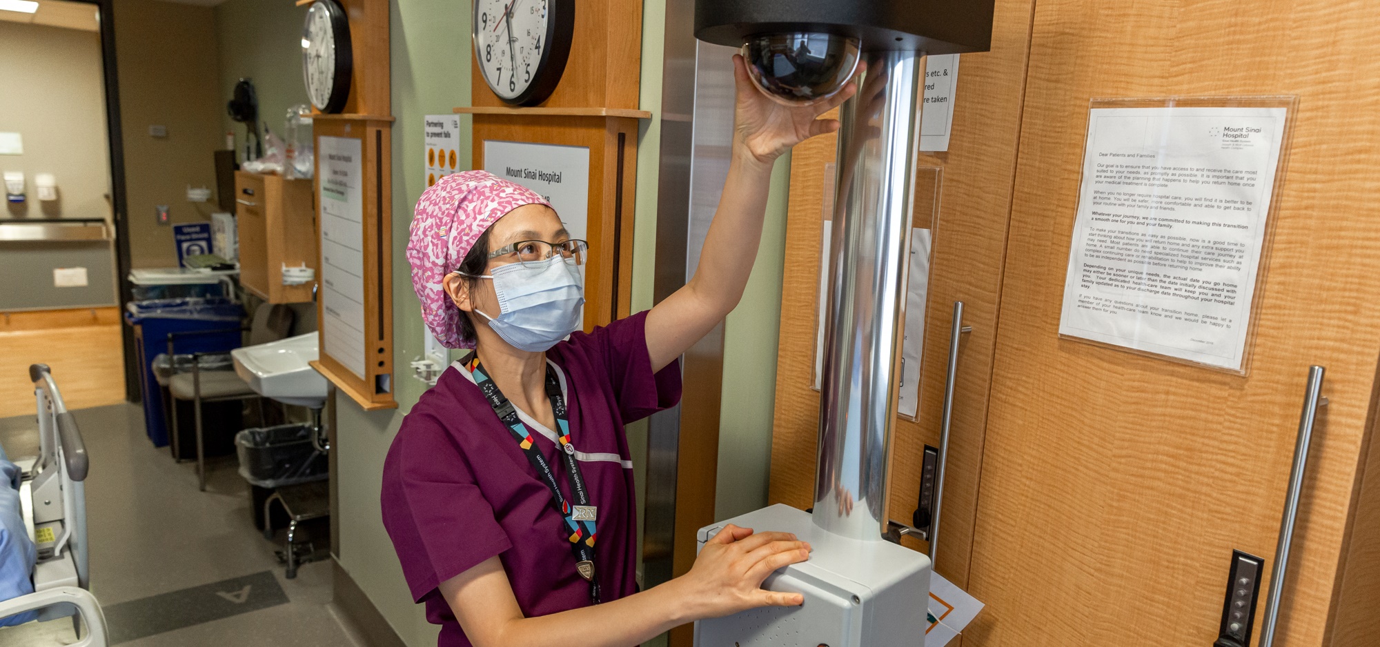 A nurse adjusts a tall mobile camera device in a patient room.