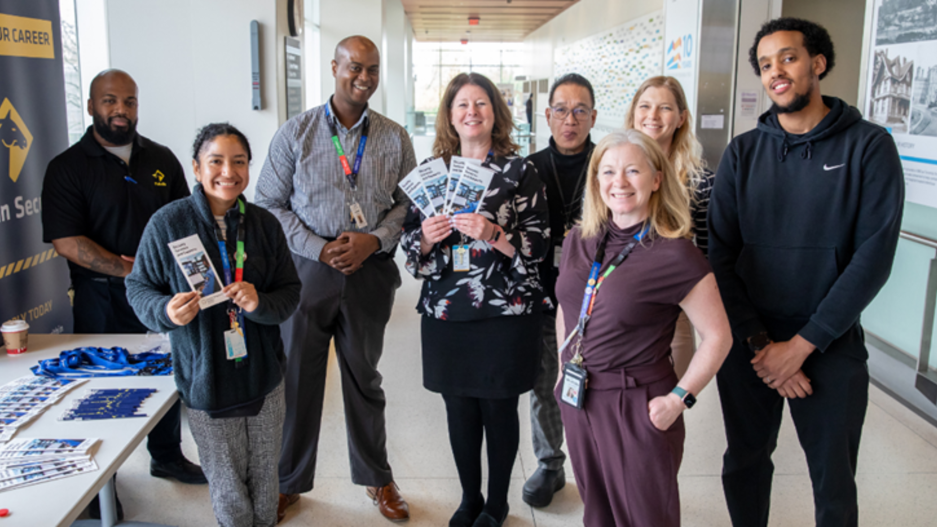 A group of eight hospital employees stands in the corridor at Hennick Bridgepoint Hospital. They are next to a table with some brochures and other information materials on display.