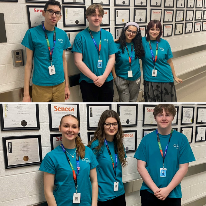 A collage of two photos of groups of people standing, smiling and looking at the camera. The photo on top has four people and the photo on the bottom has three people. They are wearing turquoise t-shirts and lanyards with badges. In both photos, the people are standing in front of a white wall that has many framed certificates on it. 