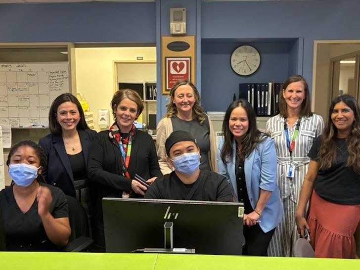 A group of hospital employees standing behind a team station desk, some are wearing scrubs