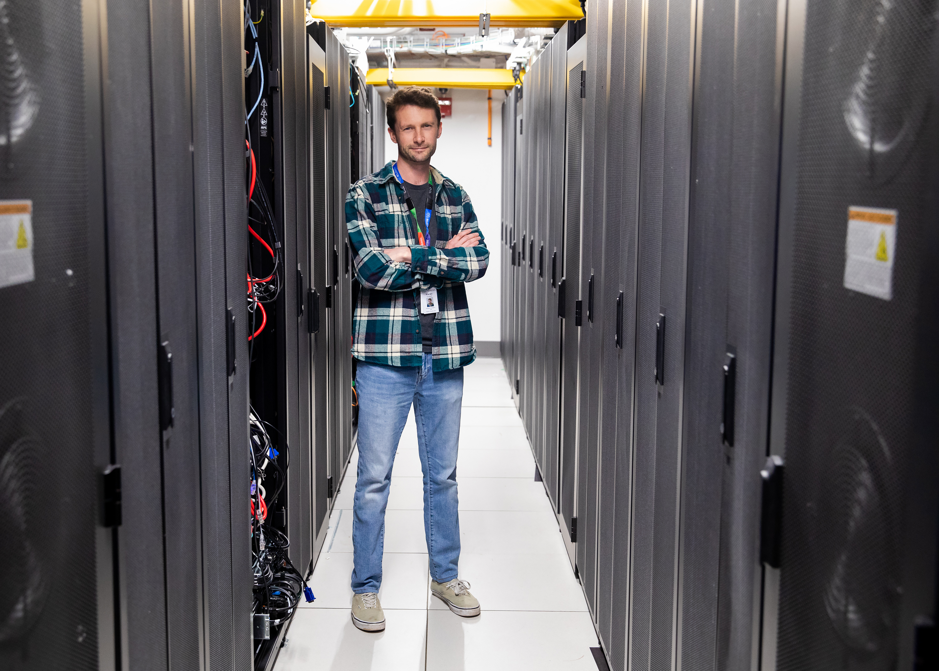 a while man wearing jeans and shirt standing in a server room