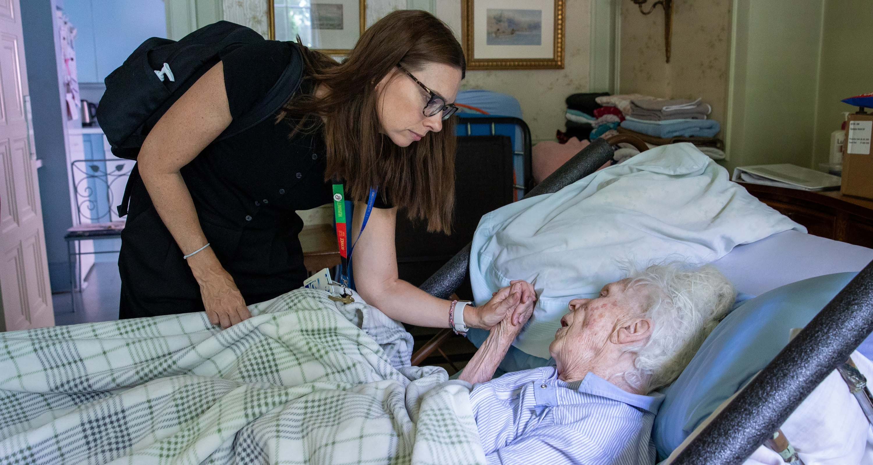 Dr. Marnie Howe holds the hand of a patient resting in bed during a palliative care at home visit.