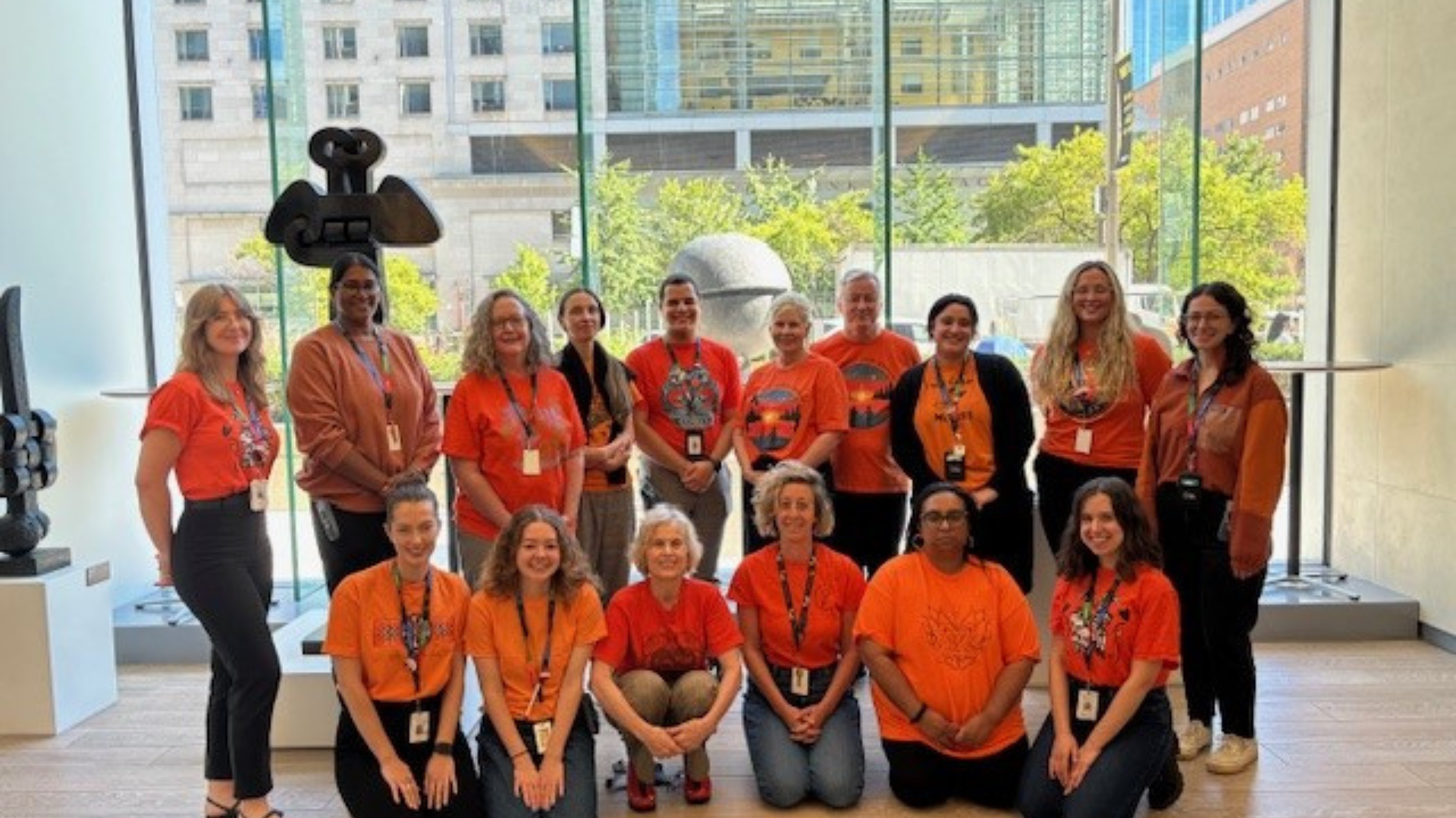 A group of people standing in rows. They are all wearing orange shirts for Orange Shirt Day. They are looking at the camera