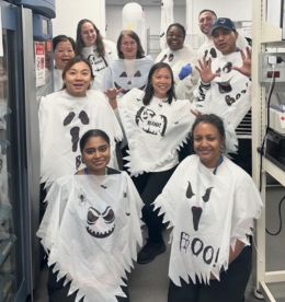 A group of people dressed with white ponchos that have ghost faces on them. They are looking at the camera smiling