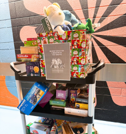 A cart piled high with various toys including items in boxes and a stuffed animal at the top