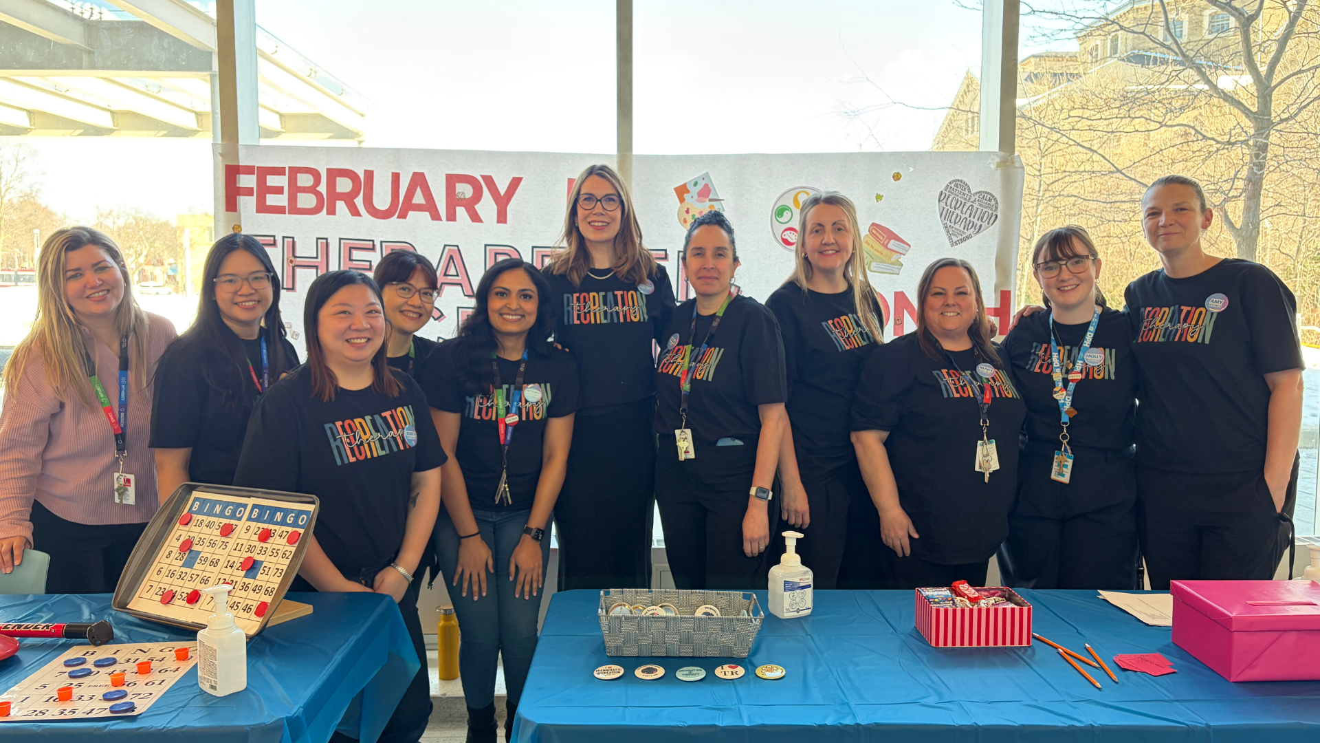 Members of the Therapeutic Recreation Team stand behind their Therapeutic Recreation Month information table at Hennick Bridgepoint. They're looking at the camera, smiling.