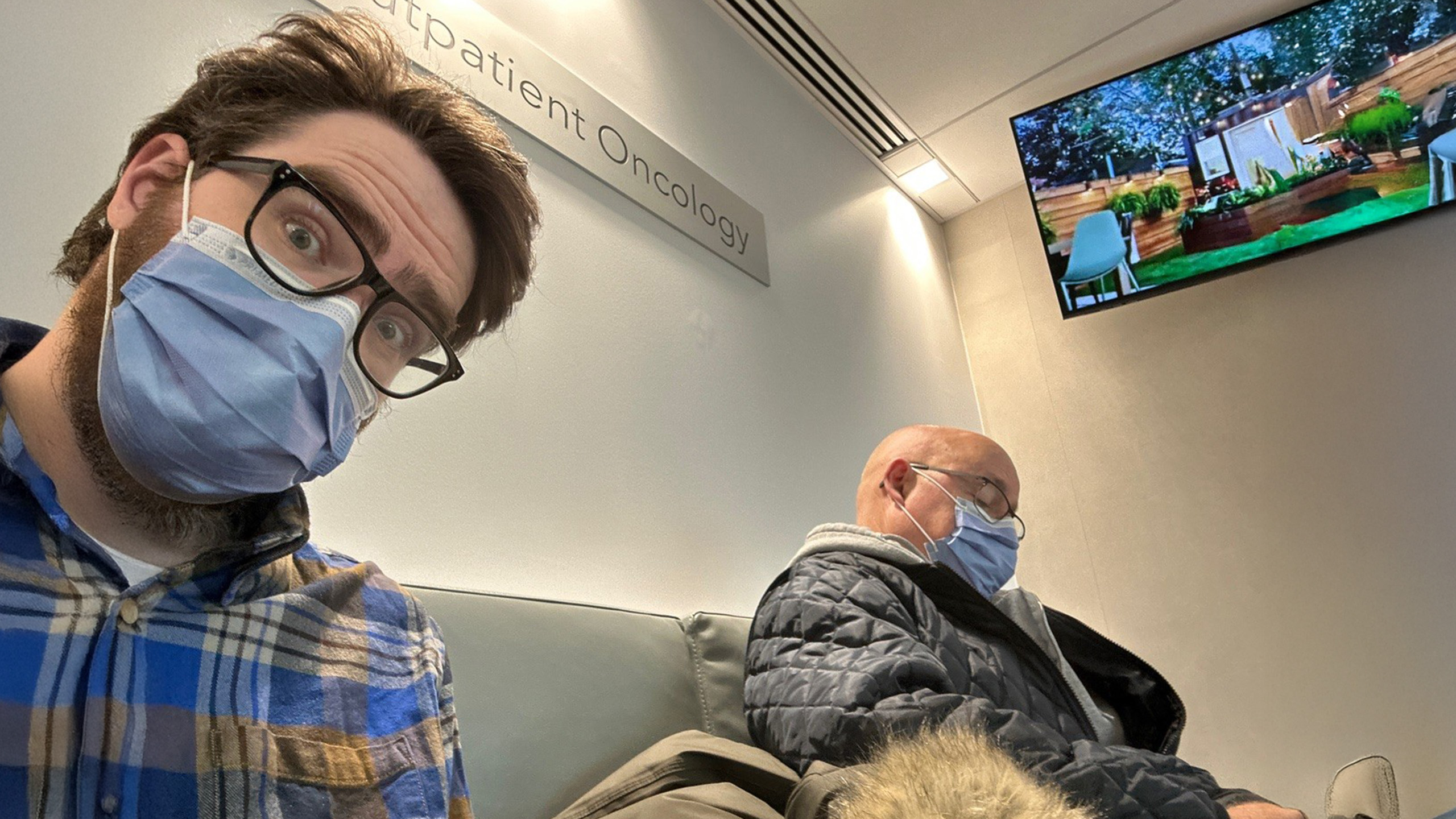 two men sit in a hospital waiting room, one is sleeping
