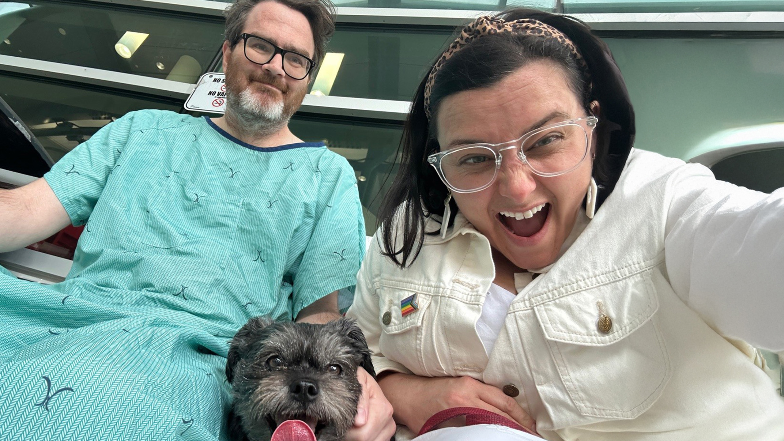 Man in hospital gown sits with woman and dog