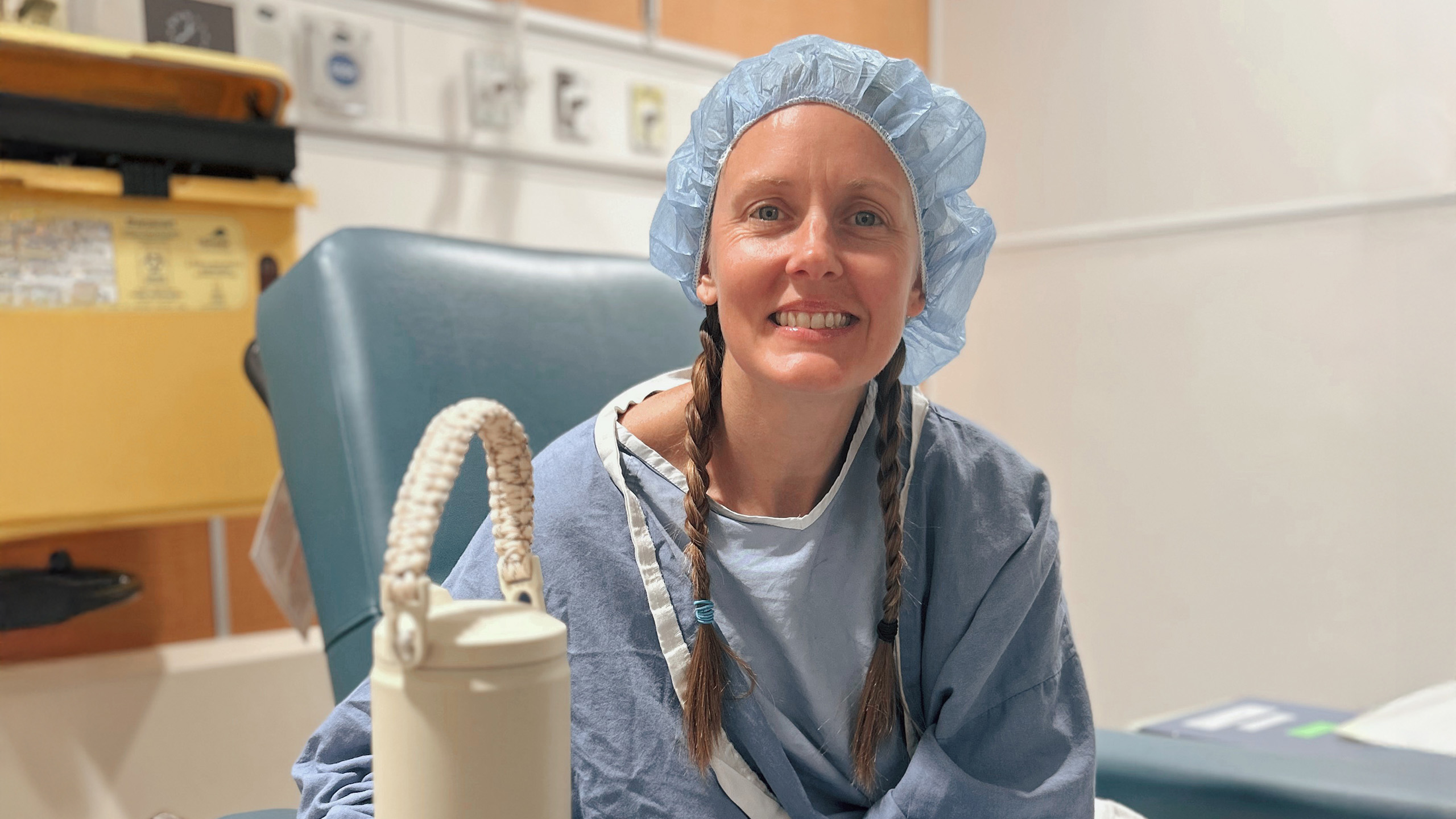 Woman sits in hospital gown and cap, ready for surgery