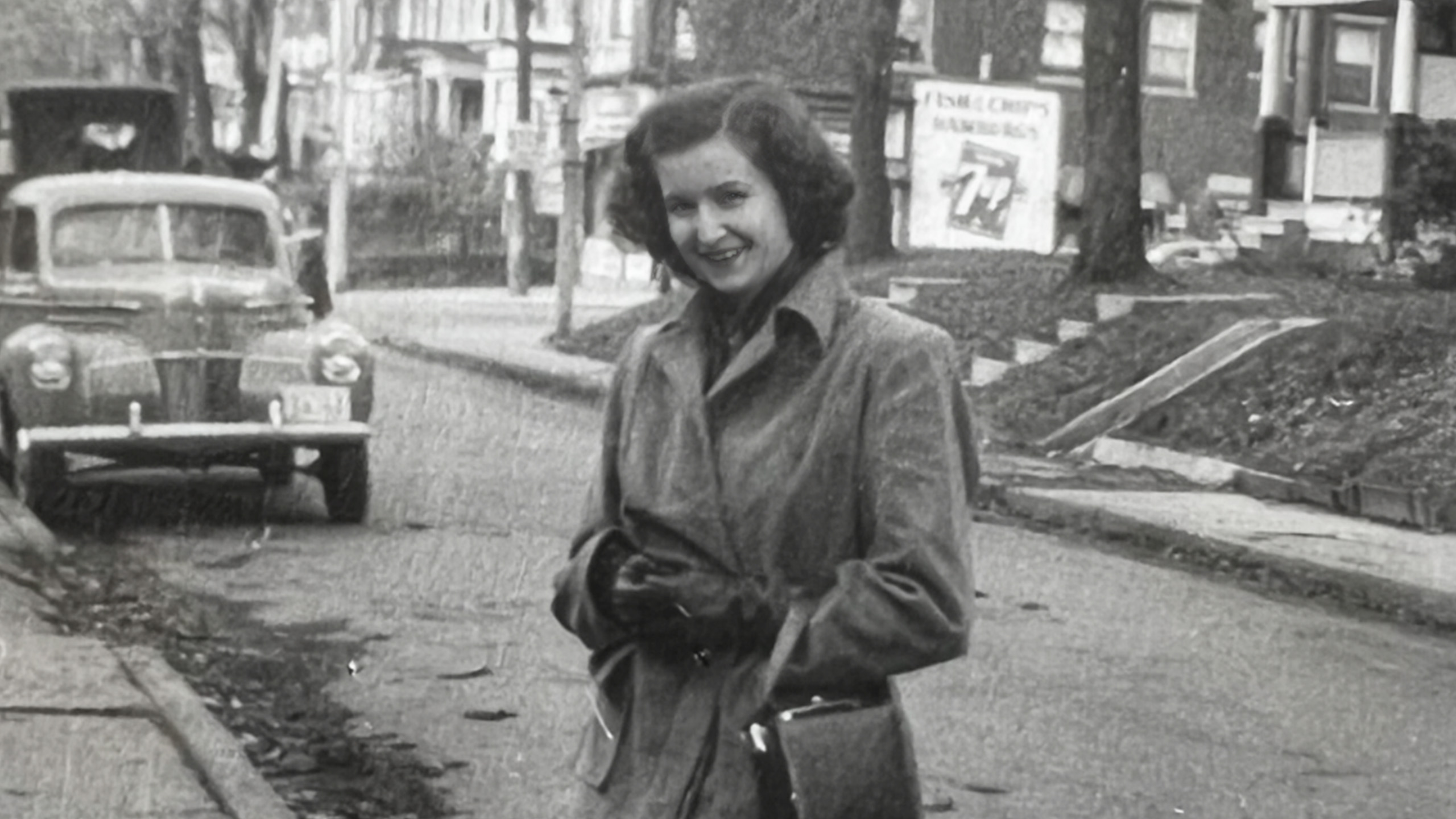 black and white photo of a young woman standing in a residential street