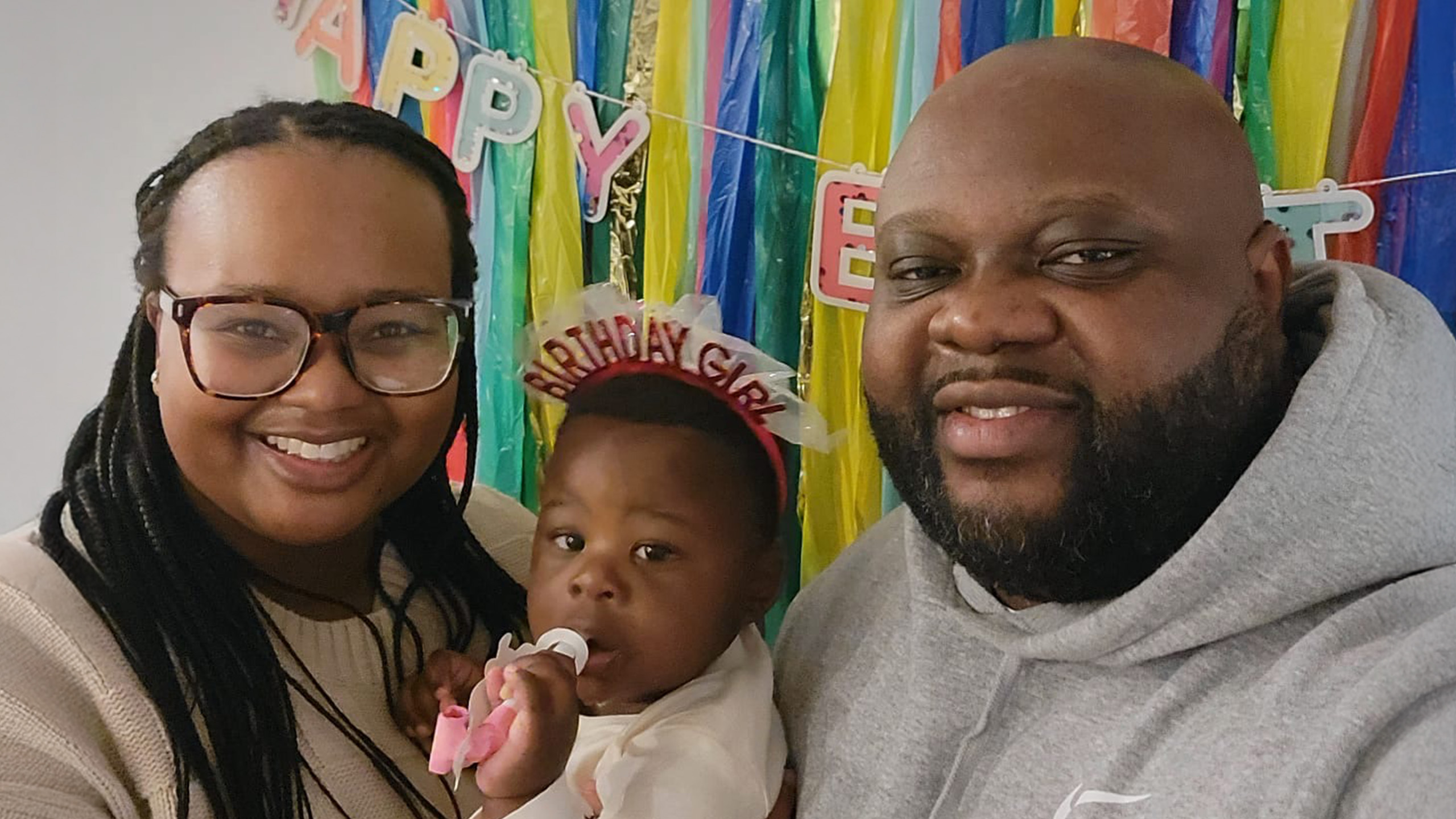 mother, father and baby smile in front of a birthday banner