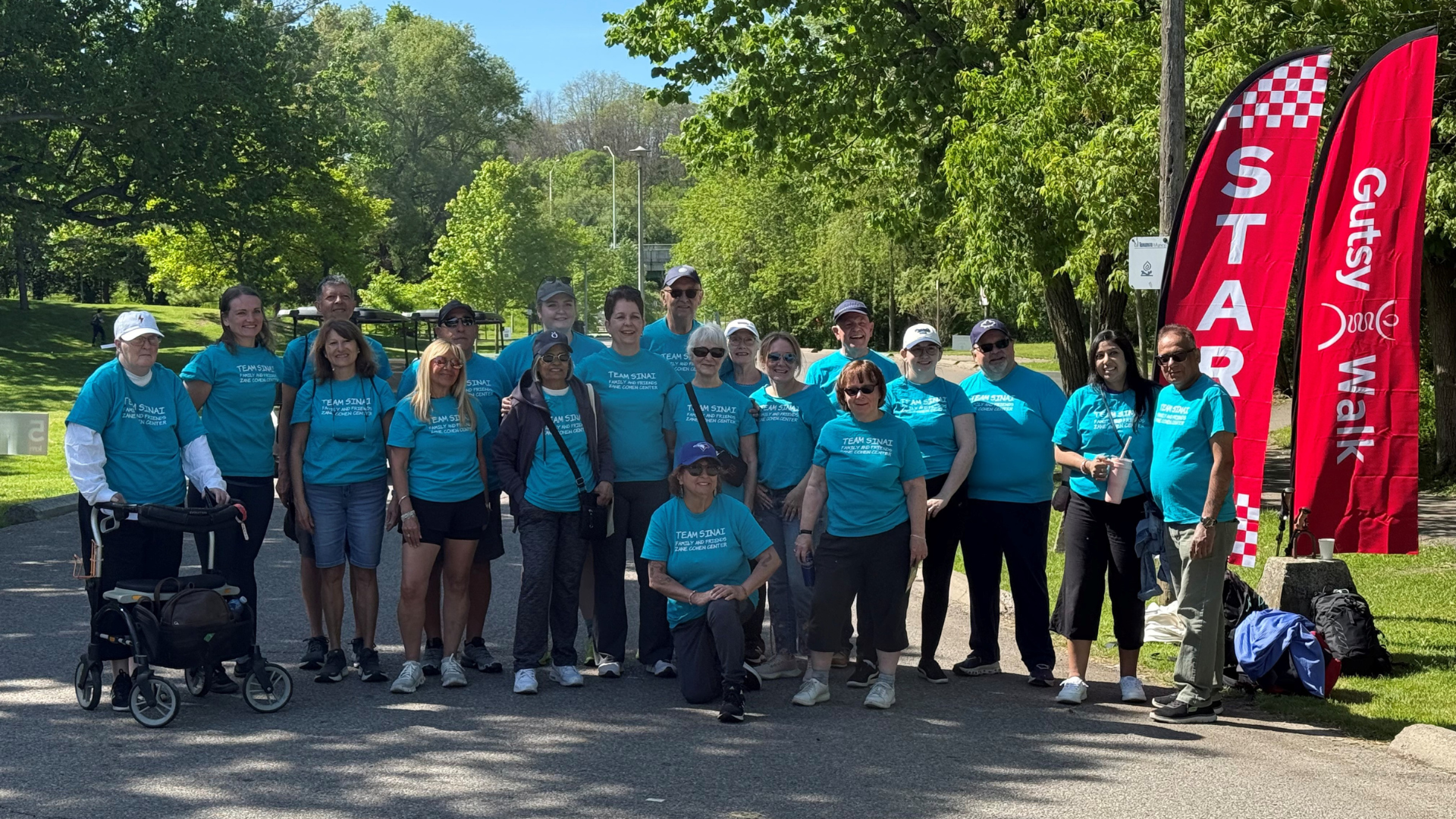 A group of people standing on a road or path in a greenspace. They are wearing matching teal t-shirts.