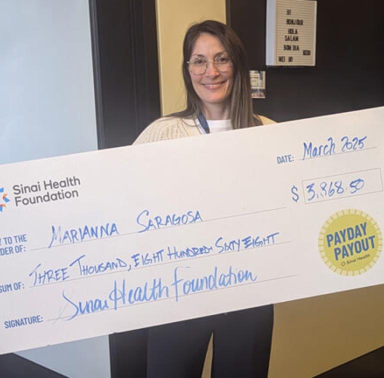 Smiling woman holds an oversized Sinai Health Foundation cheque featuring the “Payday Payout” logo