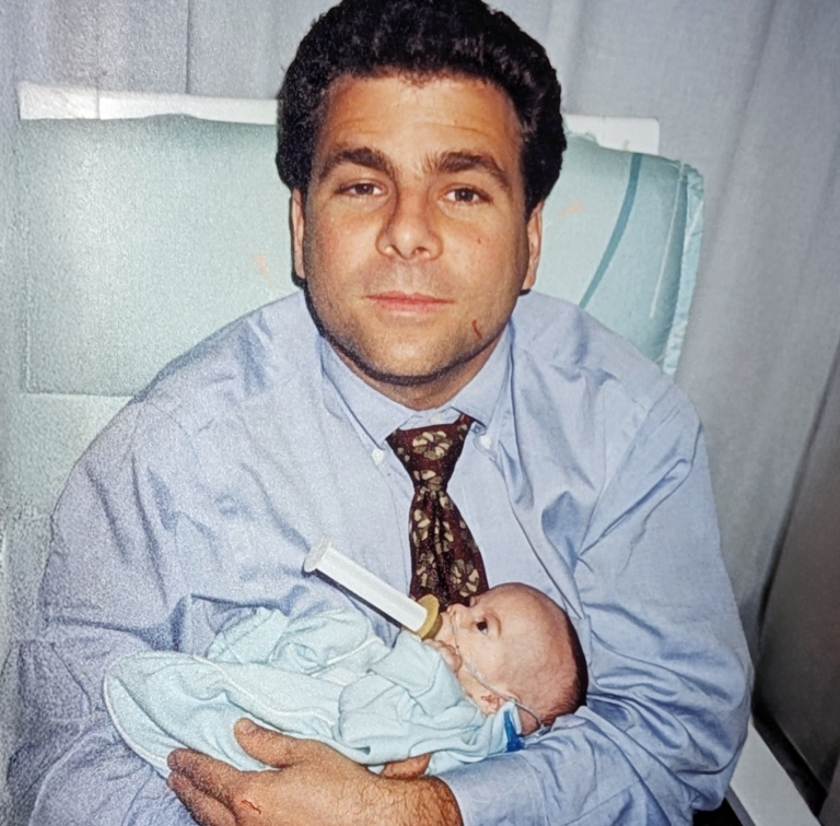man sits in hospital holding infant