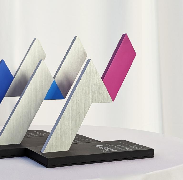 Three trophies on a table with a white table cloth 