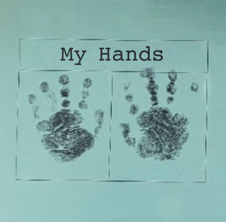 Two dark grey handprints on a pale blue piece of paper with the words My Hands printed in black above