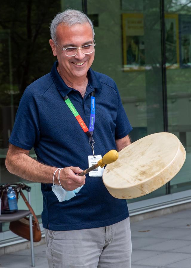 A man is smiling while holding and playing an Indigenous ceremonial drum