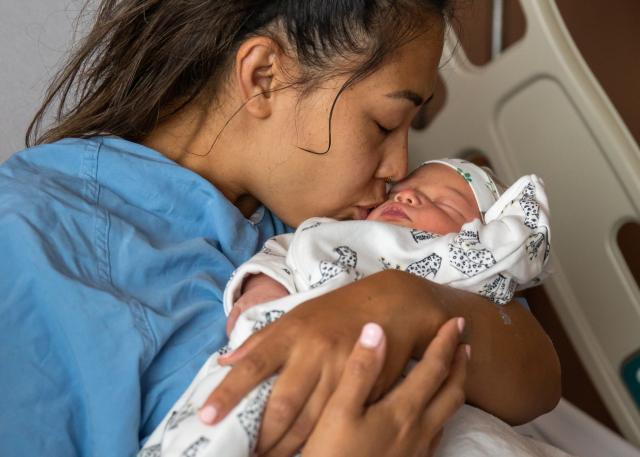 A woman sits in a hospital bed and kisses her newborn baby