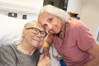 Photo shows head and shoulders of Angus and Elfie as they hold hands and pose for a photo in Angus's hospital room