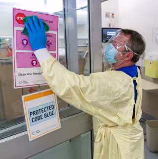 A clinical service assistant in full PPE washes the doors in Mount Sinai's Emergency Department
