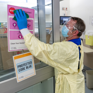 A clinical service assistant in full PPE washes the doors in Mount Sinai's Emergency Department