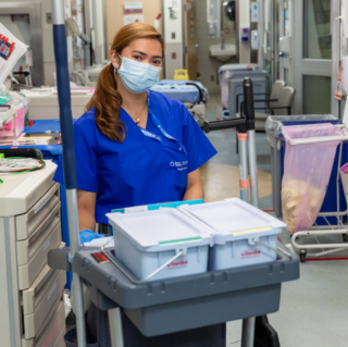 Clinical Service Assistant wearing a mask with a cleaning cart