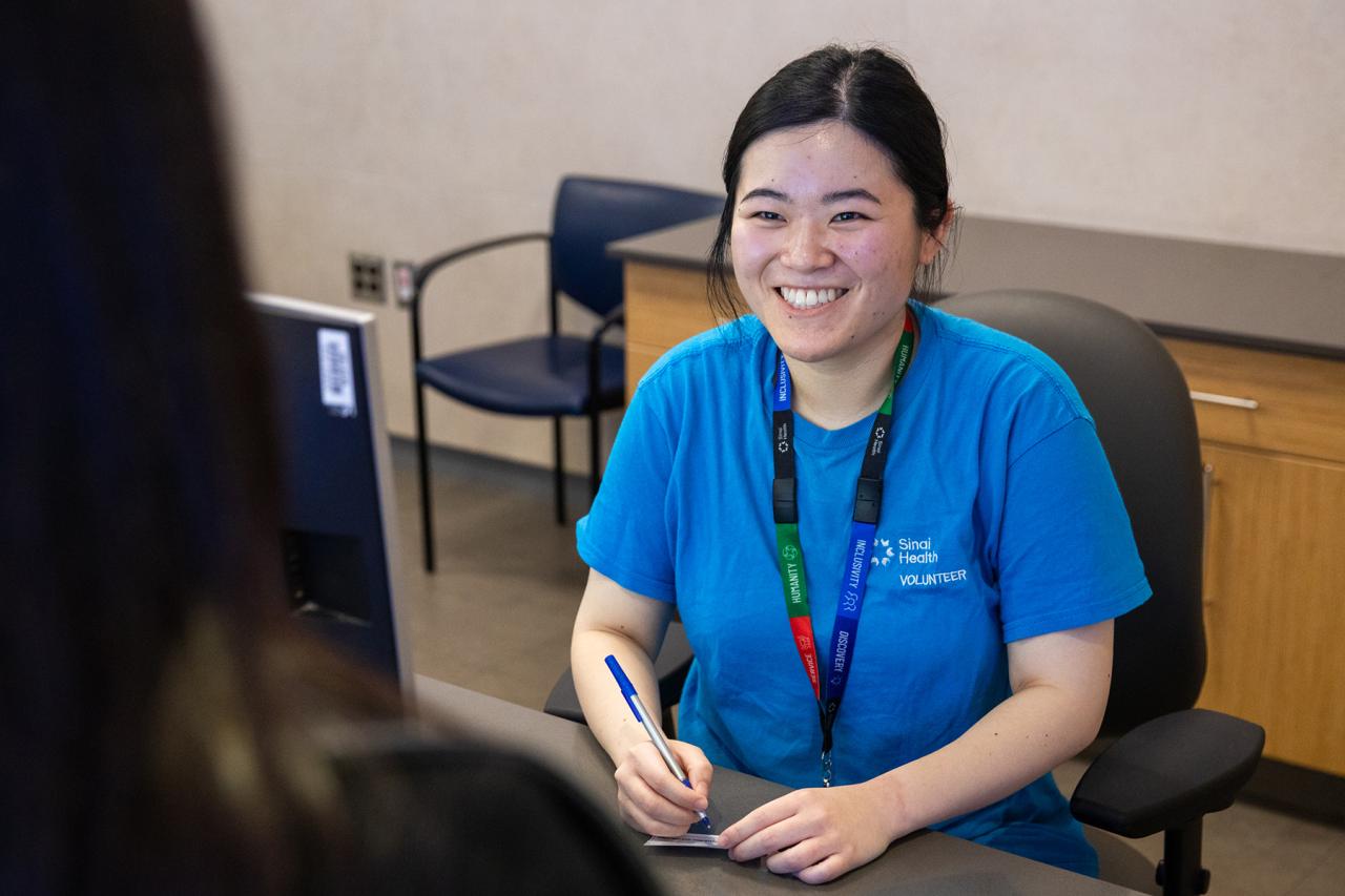 A hospital volunteer smiling while assisting a visitor at the information desk.