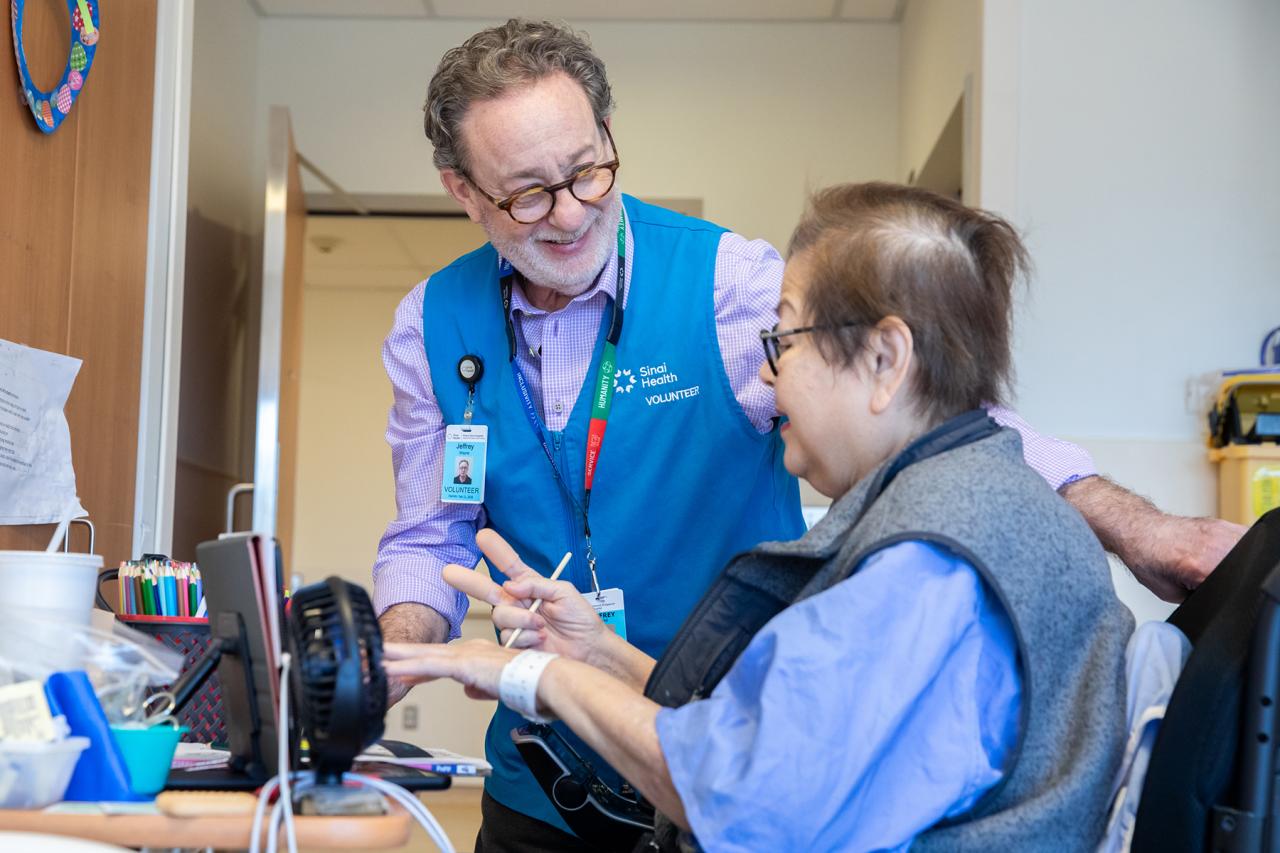 A hospital volunteer smiling while assisting a patient with an art activity.