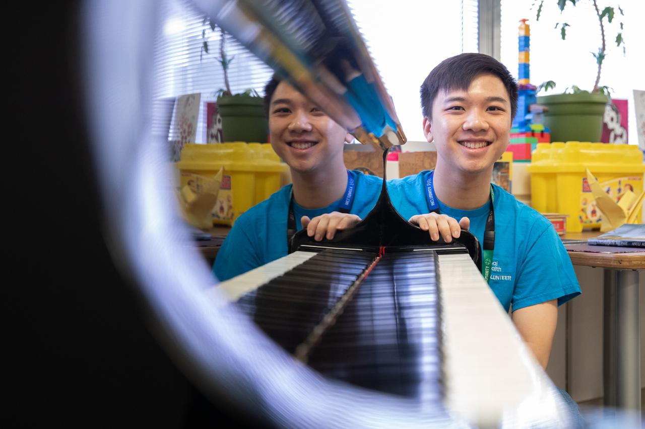 A hospital volunteer smiling at one end of a piano, with piano keys visible in the foreground.