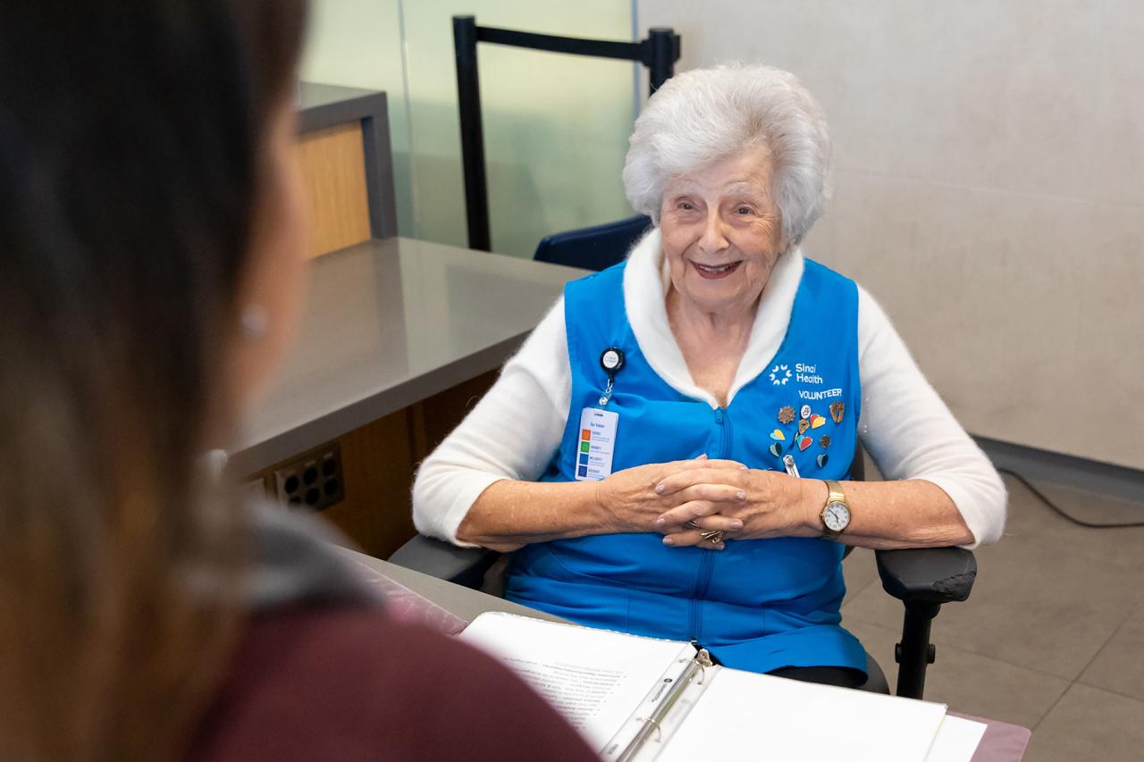A hospital volunteer smiling while assisting a visitor at the information desk.