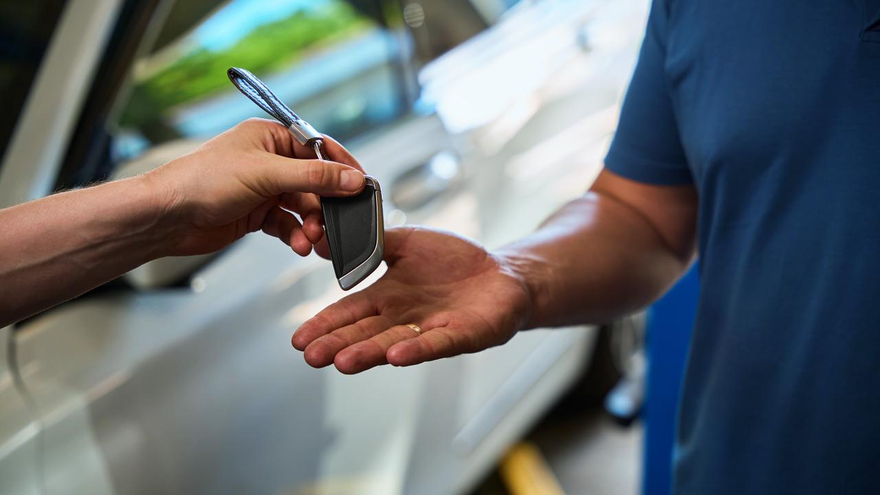 Person handing a man a set of car keys in front of a white car