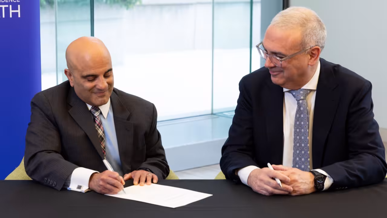 Dr. Newton and Altaf Stationwala sitting at a table signing a symbolic paper to celebrate the partnership.