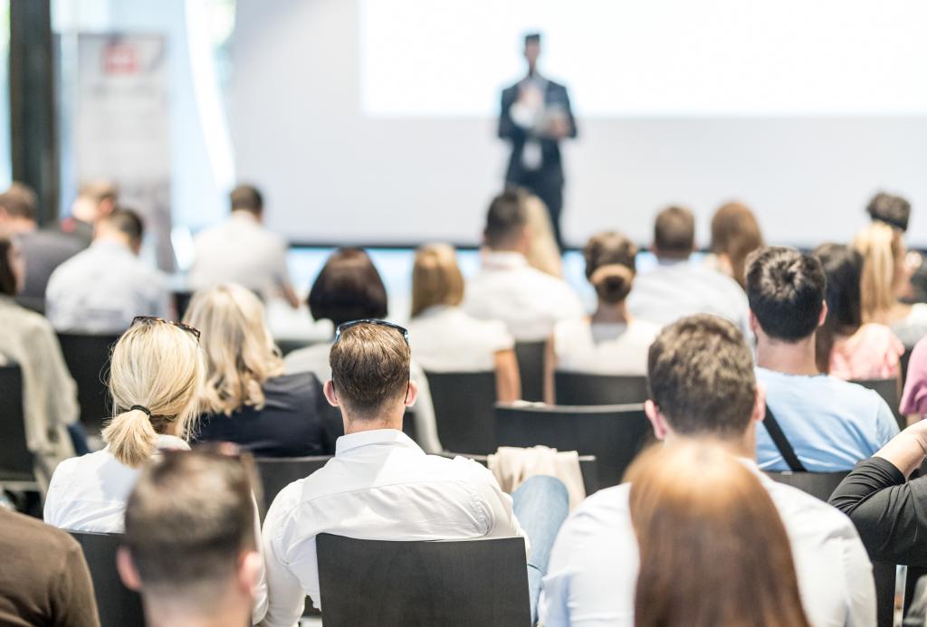 A seated audience listens to a person giving a presentation