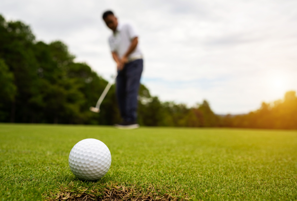 Close-up of a golf ball near the hole with a golfer putting in the background.