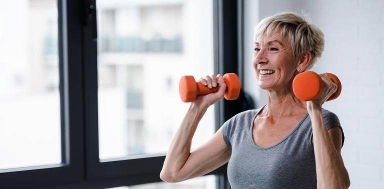 A woman lifts two orange dumbbells