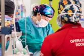 A surgeon performs surgery surrounded by three operating room staff members