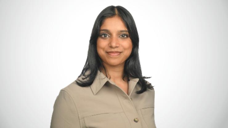 Pooja Paturi, smiling, wearing a tan button up shirt, in front of a white background