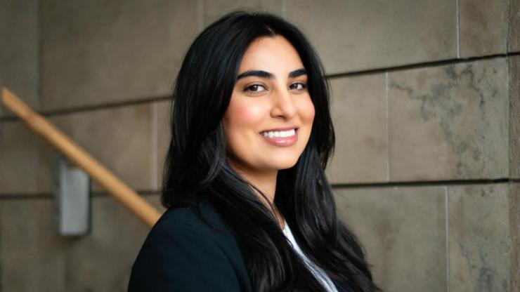 Kritika Aneja, smiling, wearing a black blazer against a grey brick backdrop