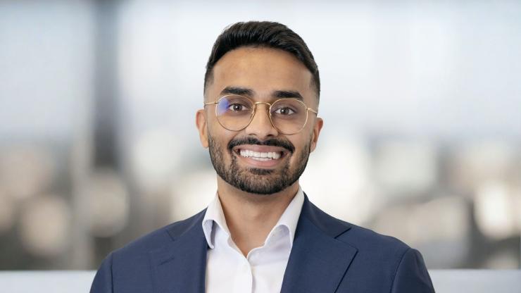 Daniel Nazareth, smiling, wearing a blue button-up shirt and blue blazer, in front of a bright office background