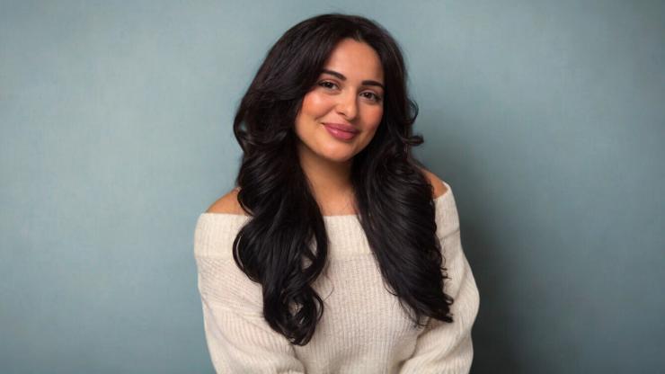 Daniela Lacaria, smiling, wearing a white sweater, in front of a blue-grey background