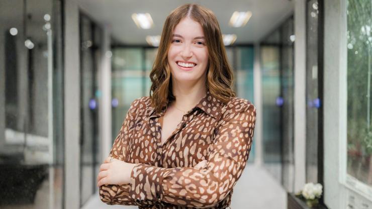 Kathryn Keenan, smiling with arms crossed, wearing a brown leopard print shirt against a bright office background