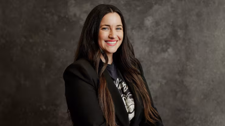 Erin Sawala, smiling, wearing a black blazer against a dark grey backdrop