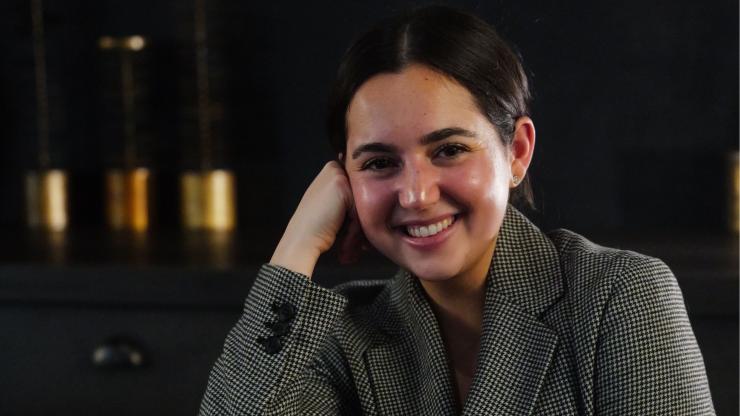 Emmy Zemel, smiling, wearing a black and white blazer, in front of a dark background