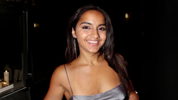 Akanksha Yeola,  smiling in a silver top in front of a dark event background