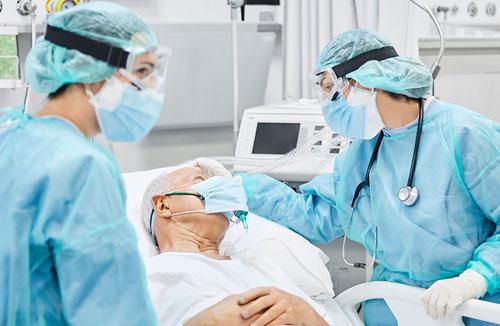 Two health care providers, wearing blue scrubs stand with a patient in the ICU