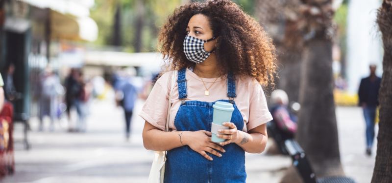 Pregnant woman is wearing a mask and holding coffee