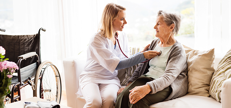 Woman listening to elderly woman's heart with stethoscope.
