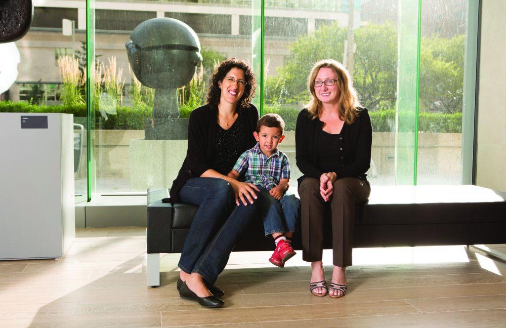 Two women sit with a young boy on a bench.