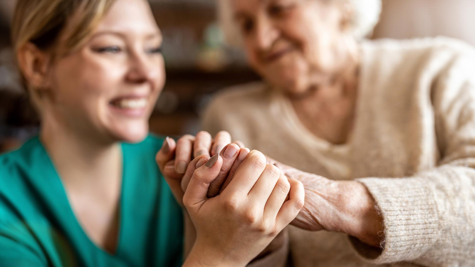 Close-up of a health care worker gently holding the hands of an older adult patient.