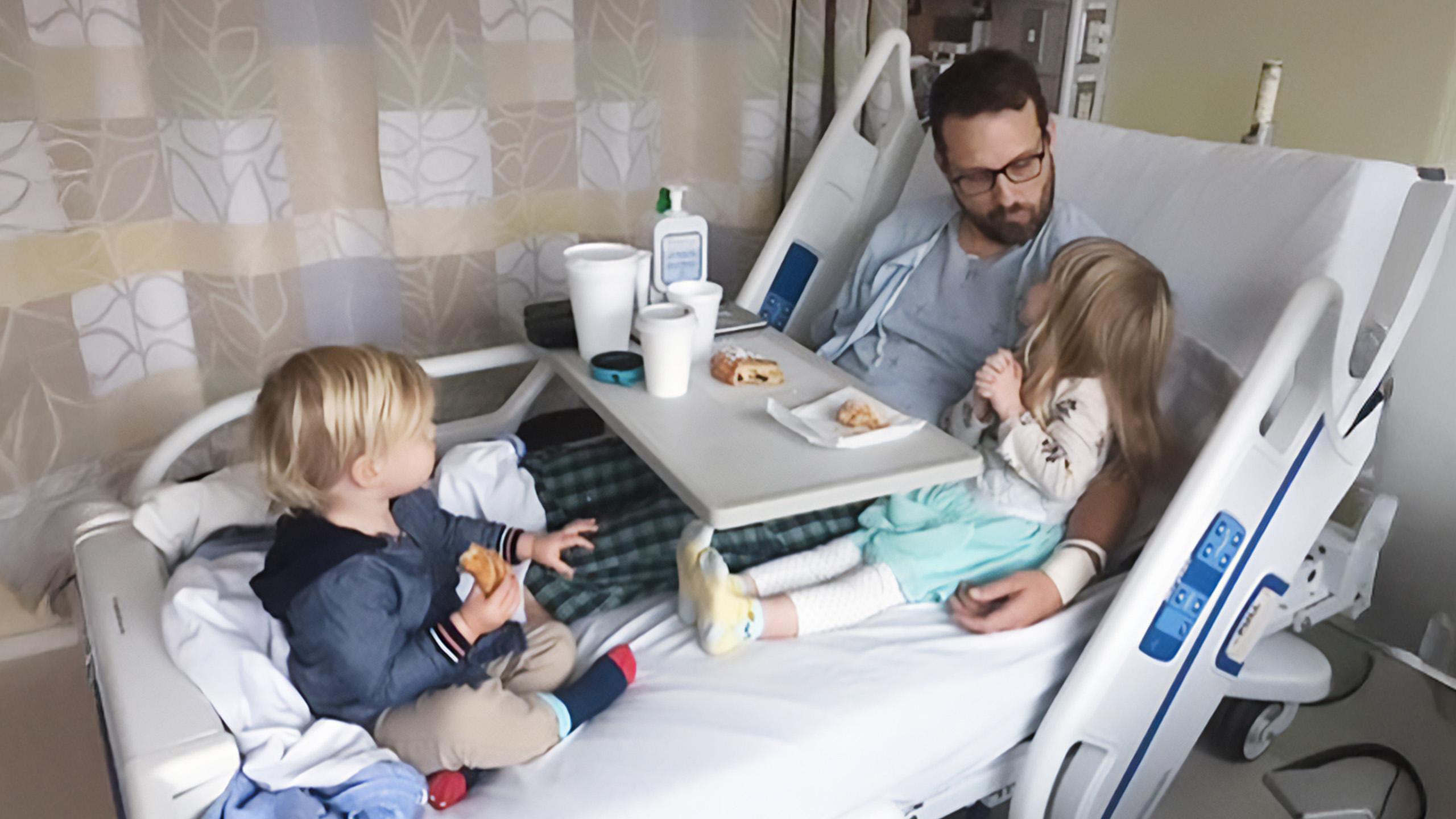 man sits in hospital bed with two young children